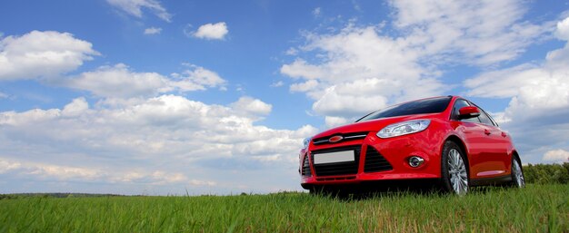 Coche rojo en un fondo del cielo azul con las nubes blancas.