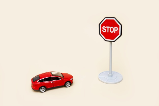 coche rojo de juguete delante de una señal de stop sobre un fondo claro con espacio para copiar