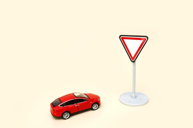 Un coche rojo de juguete delante de una señal de tráfico da paso a un fondo claro con espacio para copiar