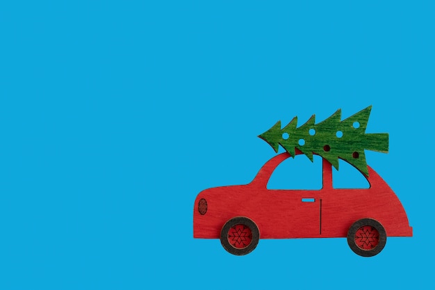 Coche rojo de madera de juguete con árbol de Navidad en el techo sobre fondo azul.