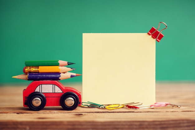 Coche rojo miniatura que lleva lápices coloridos en la tabla de madera. Concepto de regreso a la escuela