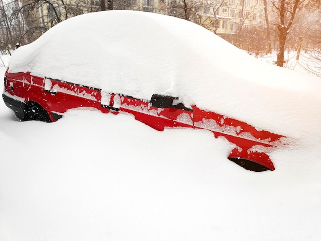 El coche rojo del sedán cubrió una gruesa capa fresca de nieve limpiando la nieve después de la tormenta de nieve del coche en el invierno