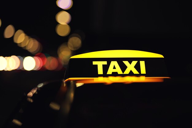 Foto coche de taxi con letrero de techo amarillo en la calle de la ciudad en el primer plano de la noche