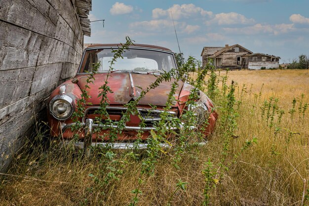 Coches antiguos abandonados en un patio con una casa abandonada en las praderas de Saskatchewan en Canadá