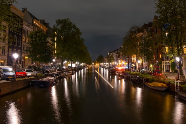 Coches y barcos estacionados en el canal de Ámsterdam por la noche