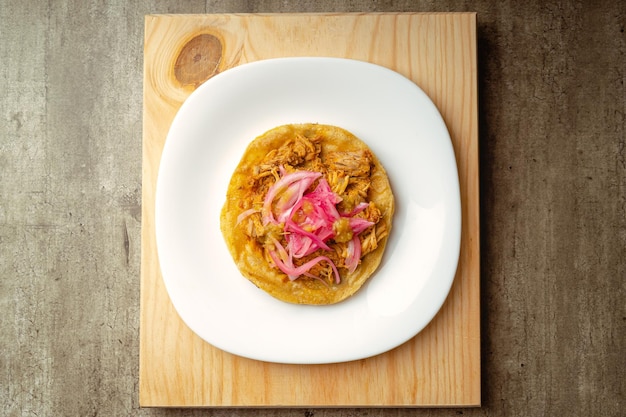 Cochinita Panuchos gourmet comida yucateca carne con cebolla roja y salsa roja picante sobre un fondo de madera