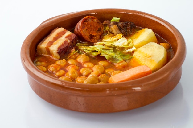 Cocido de Madrid, plato tradicional español con garbanzos. carne, embutidos y verduras, en un plato típico, aislado en blanco