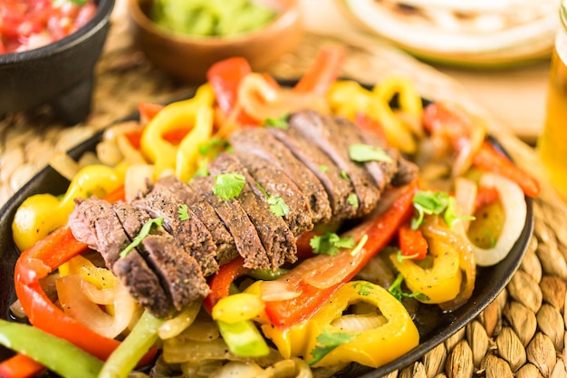 Cocina al aire libre. Filete de fajitas con pimientos morrones y cebolla amarilla en una sartén de hierro fundido para fajitas.