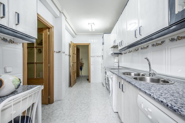 Cocina alargada con muebles altos y bajos blancos imitación piedra encimera y azulejos blancos con cenefa y gres gris en el suelo