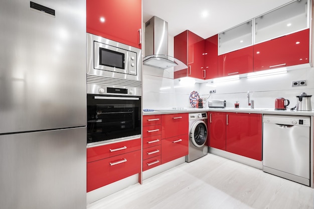 Cocina amueblada con dos paredes en forma de L con gabinetes de color rojo brillante, encimera gris y electrodomésticos de acero inoxidable integrados