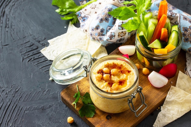 Cocina árabe Hummus de Oriente Medio con aperitivos Hummus dip con palitos de verduras frescas en una encimera de piedra oscura Espacio de copia