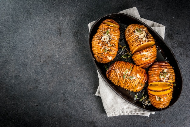 Cocina casera tradicional estadounidense. La dieta vegana. Patatas Hasselback caseras con hierbas frescas y queso. En la mesa negra, copie la vista superior del espacio