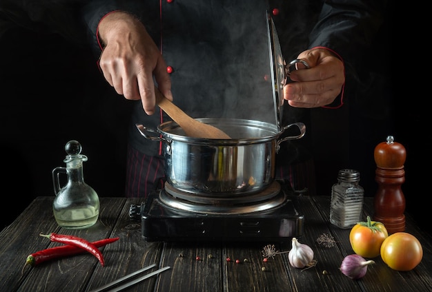 En la cocina, el chef prepara sopa dietética con las manos en una olla caliente Deliciosa comida para el almuerzo