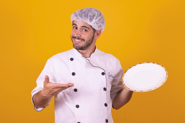 Cocina culinaria y concepto de personas chef masculino sonriente feliz en Toque sosteniendo plato vacío fondo gris amarillo