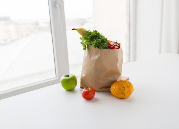 cocina, dieta, comida vegetariana y concepto de alimentación saludable: cierre de una bolsa de papel con verduras, verduras y frutas frescas y maduras en la mesa de la cocina en casa