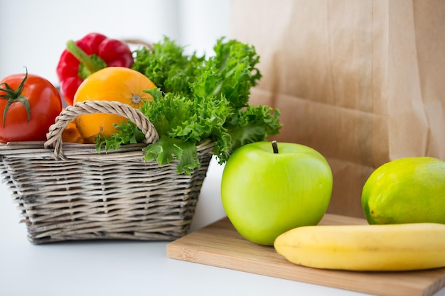 cocina, dieta, comida vegetariana y concepto de alimentación saludable: cierre de la cesta con verduras, verduras y frutas frescas y maduras en la mesa de la cocina en casa