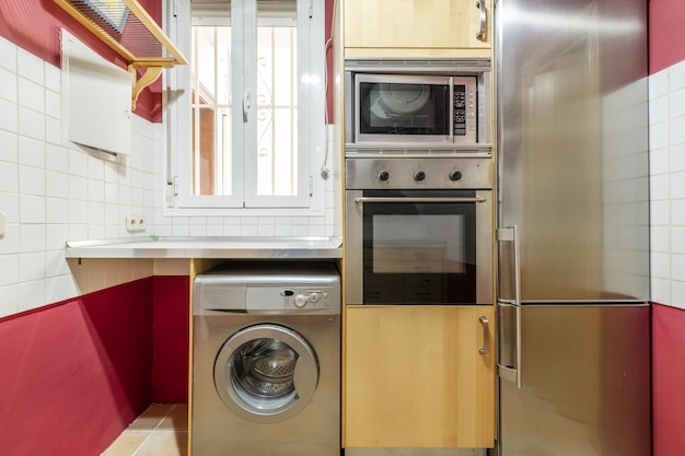 Cocina con electrodomésticos de acero inoxidable y nevera a juego con encimeras de metal, paredes con azulejos blancos y pintura roja.