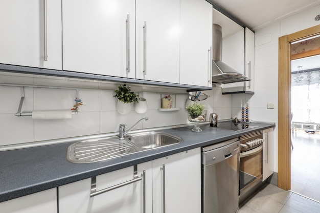 Cocina con gabinetes blancos con cornisas y encimeras grises y electrodomésticos de acero inoxidable integrados