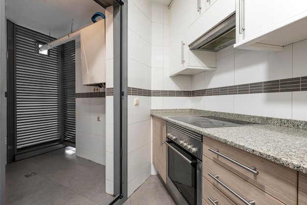 Cocina con gabinetes blancos, encimeras de granito blanco y negro, azulejos blancos y molduras marrones combinadas con electrodomésticos de acero inoxidable