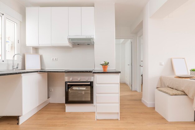 Foto cocina con gabinetes blancos, puertas y cajones, electrodomésticos empotrados, encimeras negras y pisos de madera