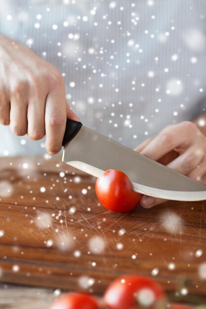 cocina, gente, comida vegetariana y concepto de hogar - cerca de un hombre cortando tomate en una tabla de cortar con un cuchillo grande