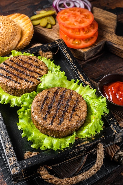 Cocina Hamburguesas sin carne a base de plantas con chuletas, hamburguesas, tomate y cebolla asados sin carne vegetariana en una bandeja de madera para servir. Fondo de madera. Vista superior.