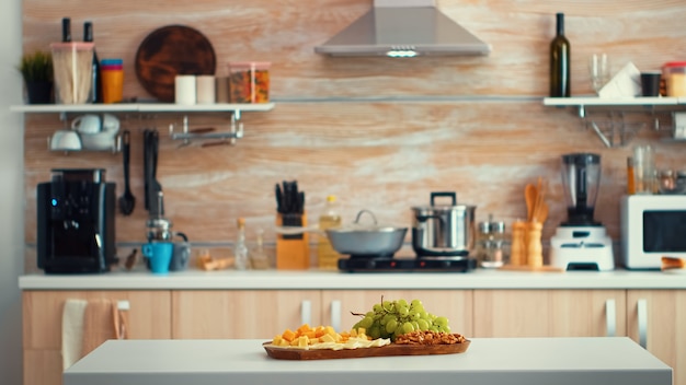 Cocina moderna vacía con uvas en la mesa. Interior de sala de cocina de espacio abierto con luz natural y fondo borroso. Diseño de decoración residencial de arquitectura de lujo con mesa de comedor en medio de th