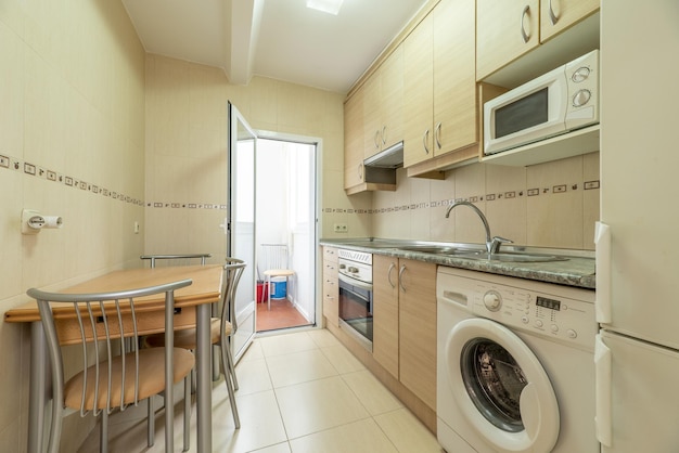 Cocina con muebles de madera de abedul con tiradores metálicos una encimera de aspecto pétreo con electromesivos integrados de azulejos amarillos de varios colores y un perchero con puerta de aluminio blanco y cristal