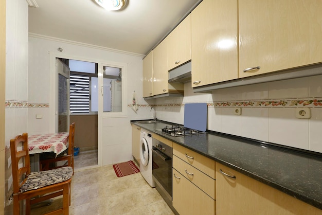 Cocina con muebles de madera encimera negra lavadora blanca mesa de madera con sillas a juego y salida a terraza tendedero