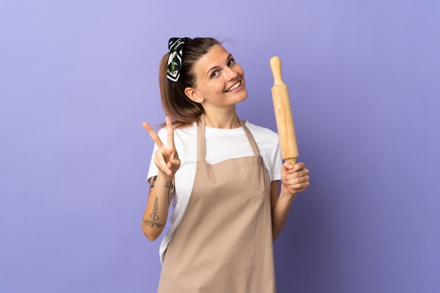 Cocina mujer eslovaca aislada en la pared púrpura sonriendo y mostrando el signo de la victoria