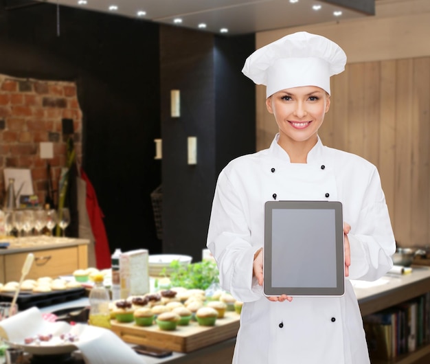 cocina, panadería, gente, tecnología y concepto de comida - chef, cocinera o panadera sonriente que muestra la pantalla en blanco de la computadora de la tableta sobre el fondo de la cocina del restaurante