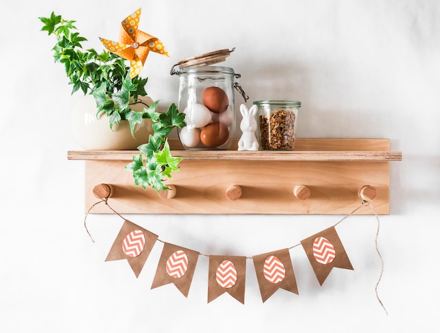 Cocina de Pascua decoración interior bodegón Estante de madera con una flor casera huevos de conejos de cerámica y guirnalda de Pascua de papel casera sobre un fondo claro