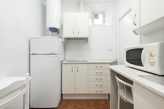 Cocina pequeña con gabinetes blancos con calentador de agua, nevera blanca y horno de microondas