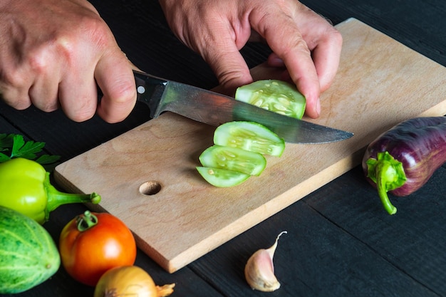 En la cocina del restaurante, el chef está cortando pepino maduro para ensalada Primer plano de las manos del cocinero durante el trabajo