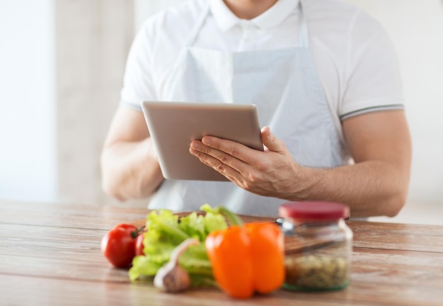 cocina, tecnología y concepto de hogar - primer plano del hombre leyendo la receta de la computadora de la tableta