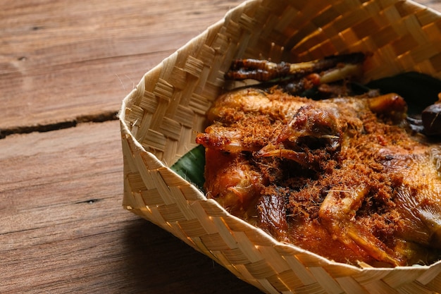 Cocina tradicional de Indonesia. Ayam goreng kalasan en una caja de bambú tejido sobre mesa de madera