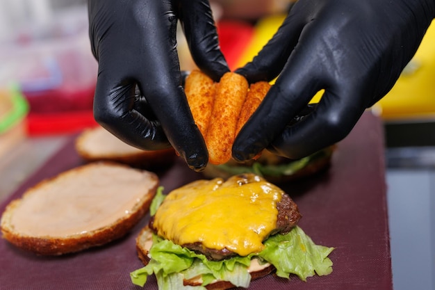 Foto cocinando una hamburguesa con queso el cocinero pone palitos de queso en una chuleta con queso