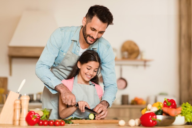Foto cocinando con papá niña feliz preparando la cena con su padre en la cocina haciendo ensalada de verduras gratis