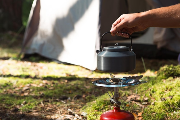 Cocinar calentar una tetera turística en un quemador de gas portátil con un cilindro de gas rojo Camping un hombre cocina el desayuno al aire libre Actividades de verano al aire libre