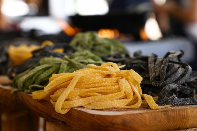Cocinar de cerca la pasta tagliatelle italiana tradicional hecha a mano fresca, pasado negro, verde y clásico sin cocer en la mesa de madera, vista de ángulo alto