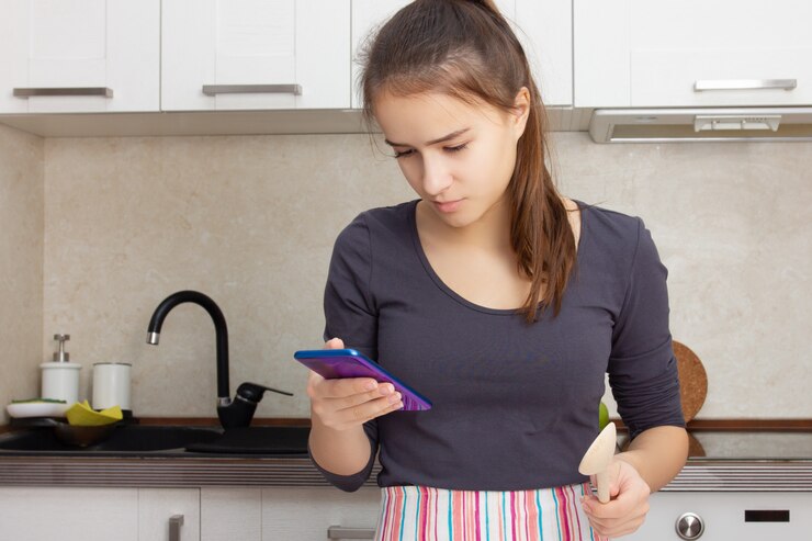 Foto cocinar comida deliciosa. niña lee una receta en un teléfono inteligente en la cocina.