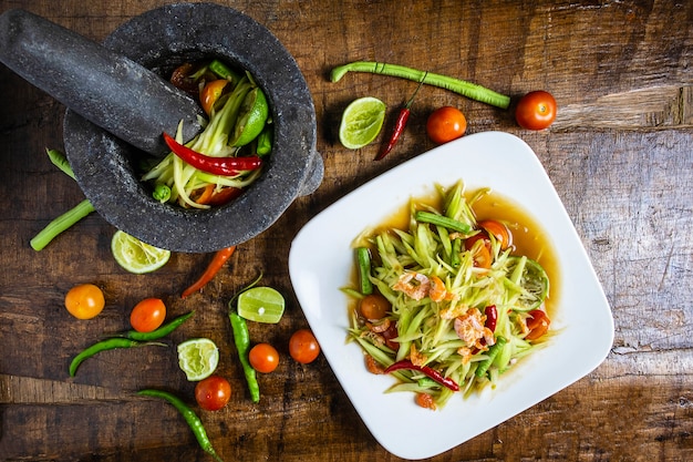 Cocinar comida tailandesa, ensalada de papaya y ensalada de papaya en un plato con una porción en una mesa de madera.