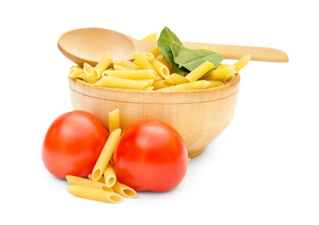 Foto cocinar comida tazón de madera con pasta cruda, espinacas, tomates y cuchara de madera sobre blanco