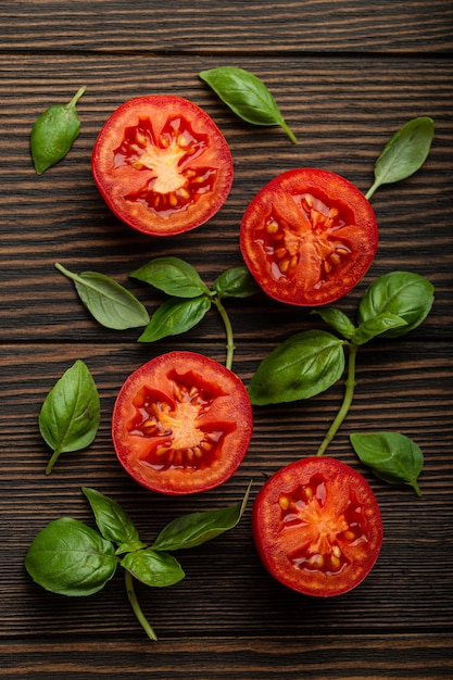 Cocinar el concepto de fondo de ingredientes alimentarios, patrón. Cortar el tomate rojo fresco y las hojas de albahaca verde sobre fondo rústico de madera, primer plano, vista superior