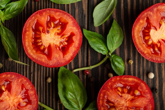 Cocinar el concepto de fondo de ingredientes alimentarios, patrón. Cortar el tomate rojo fresco y las hojas de albahaca verde sobre fondo rústico de madera, primer plano, vista superior