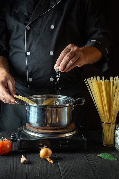 Cocinar espaguetis italianos en la cocina del restaurante El chef agrega sal a la olla de agua hirviendo