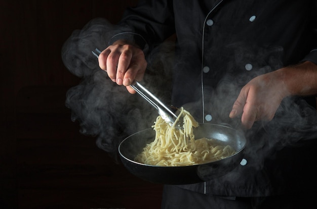 Cocinar espaguetis en una sartén en manos de un chef Espacio para publicidad sobre un fondo negro