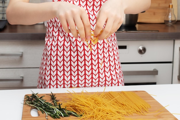 Cocinar fideos de pollo saludables y saludables Las manos femeninas rompen los espaguetis en pedazos