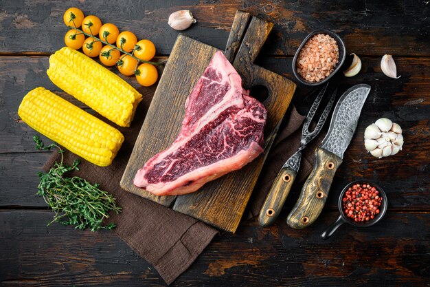 Cocinar el fondo de la carne. Chuletón de ternera añejada cruda, con especias y hierbas para parrilla, sobre fondo de mesa de madera oscura vieja, vista superior plana