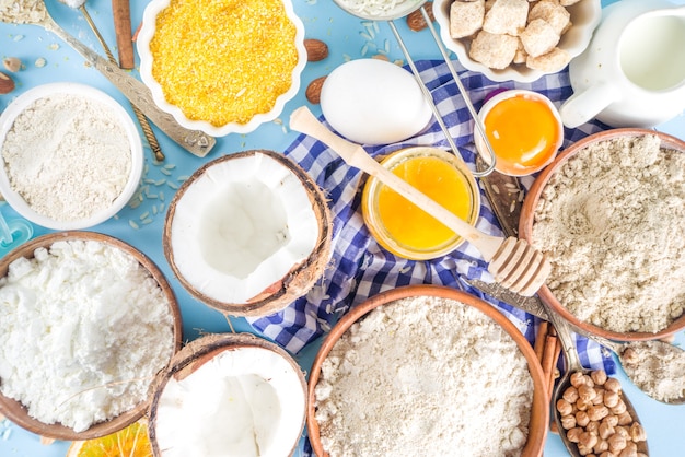 Cocinar el fondo del marco del fondo de la hornada. Selección de diversos ingredientes y harina sin gluten, para panadería dulce y de pan, en la mesa de la cocina azul colorida con utensilios, huevos, azúcar, canela